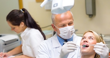 Dentist inspecting female patient’s teeth during checkup 