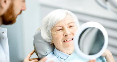 An older woman looking at her teeth in the mirror