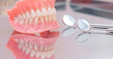 Full dentures sitting next to dental exam mirrors 