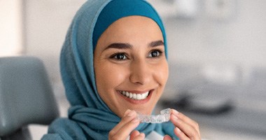 a woman holding Invisalign aligners and smiling 