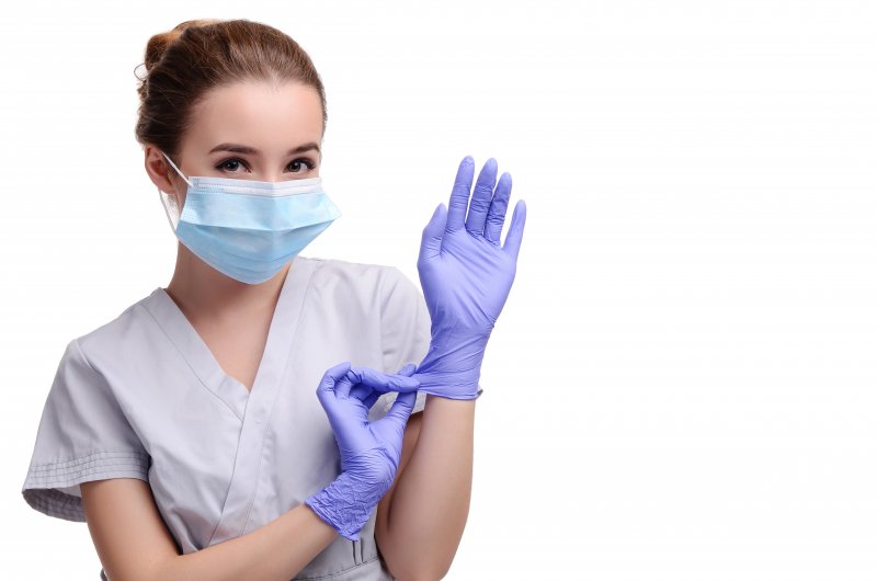 A dental professional putting on gloves and wearing a face mask