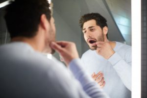 man with gum disease looking at his receded gums in the mirror 
